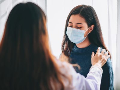 Asian doctor visit and examines on young adult woman at hospital with office syndrome and depression. The doctor checking up and consulting for health care, wearing a mask to protect covid-19 pandemic