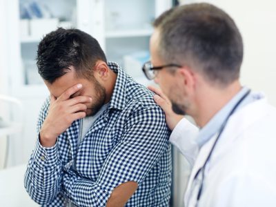 Worried patient hiding his face while doctor reassuring him