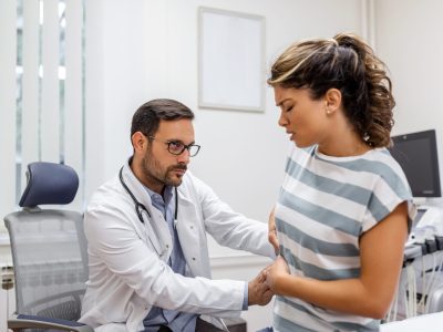 Patient telling physician about her pain and health problems during visit to hospital. Young woman complaining about back or kidney ache while sitting on examination bed at the doctor's office